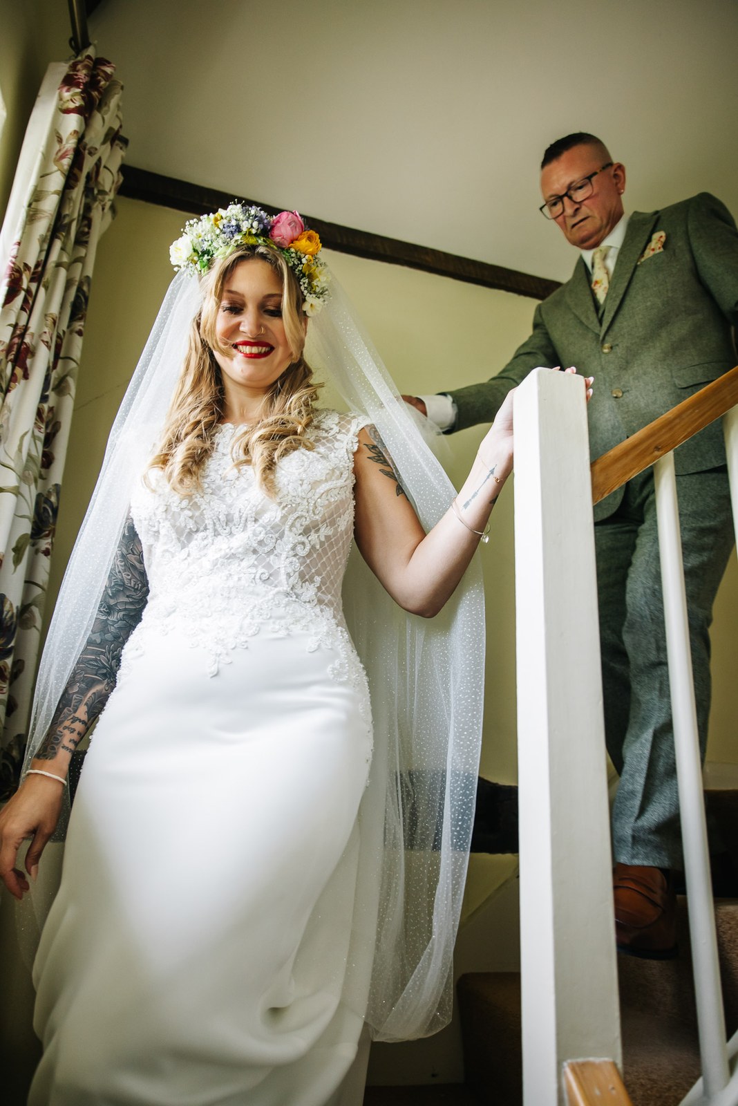 Bride coming down a staircase as her father holds her veil