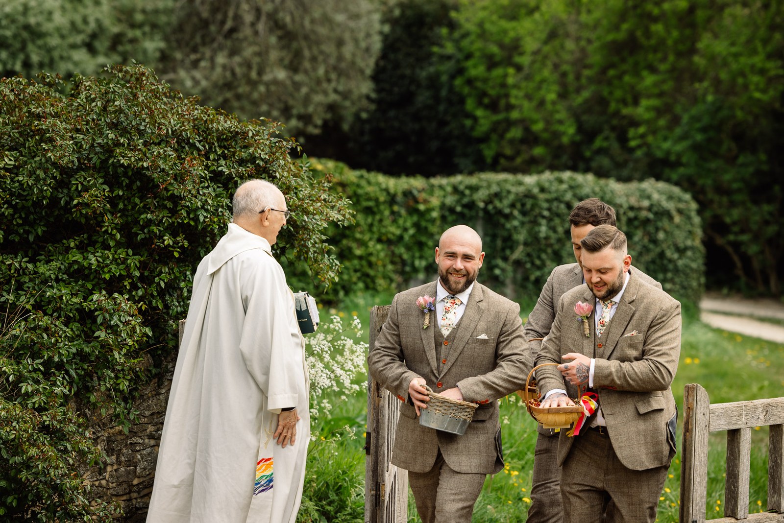 The vicar greeting groomsmen holding petal baskets outside the church