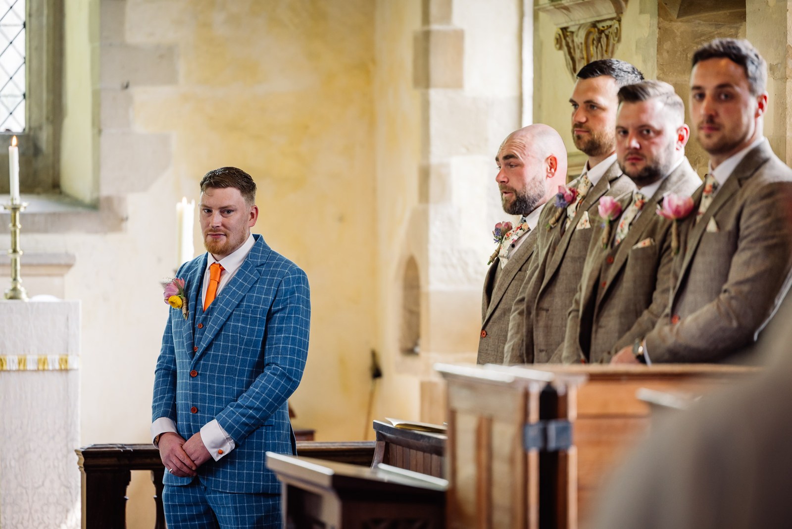 Groom in a blue check suit waiting at the front of the church, groomsmen behind