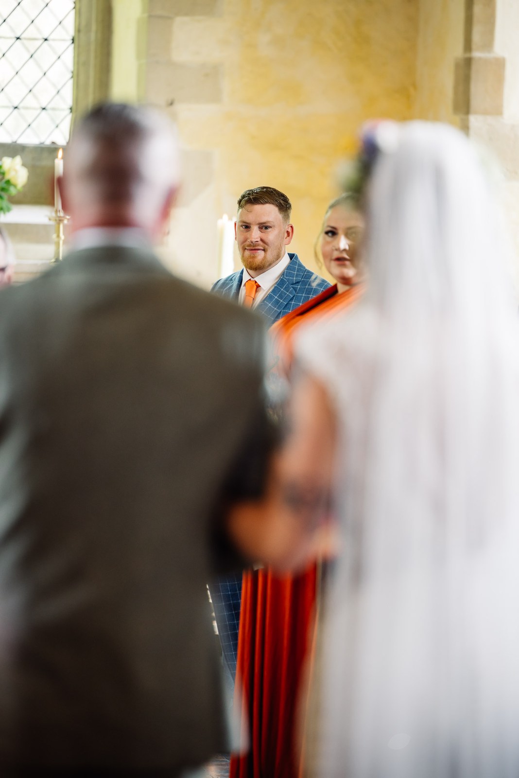 The groom waiting at the front of the ceremony, the bride's veil in the foreground
