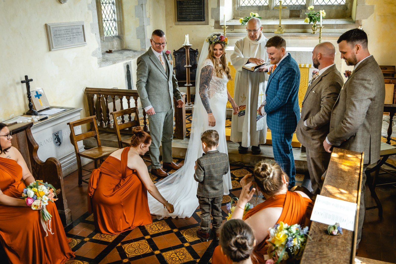 A bridesmaid arranging the bride's train as a page boy looks on during the ceremony