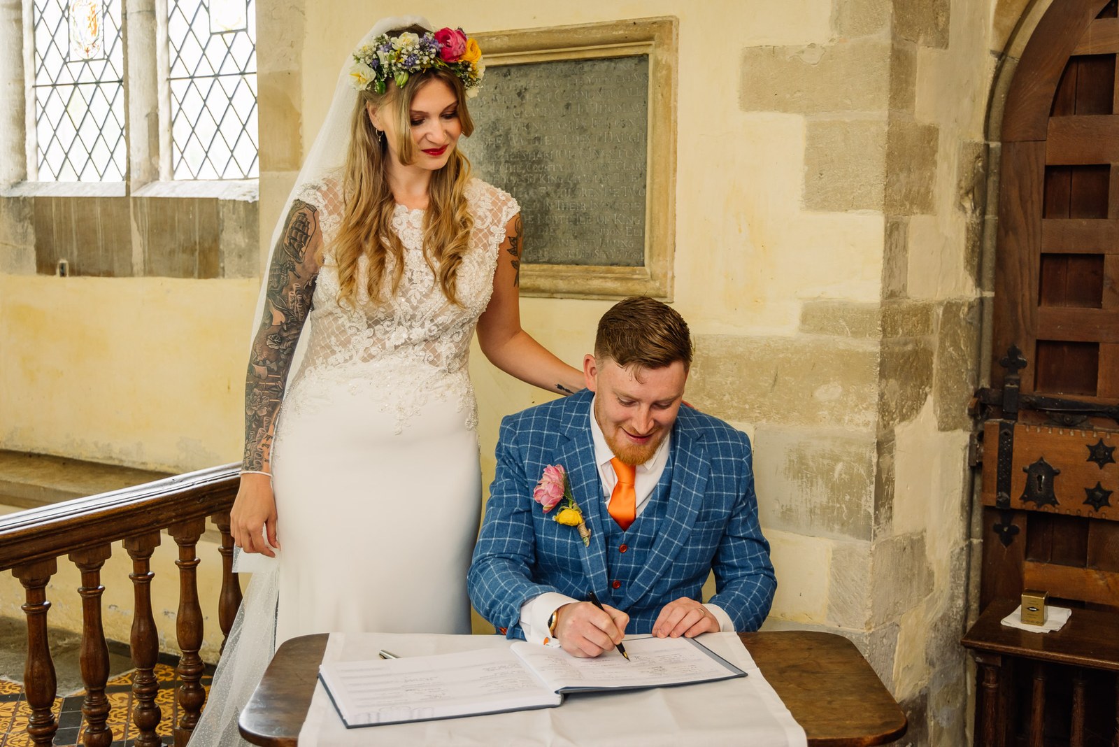 Bride standing behind the groom as he signs the register