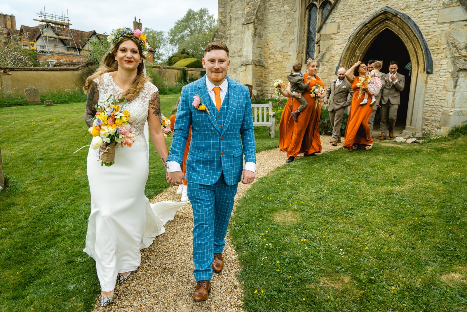 Bride and groom walking hand in hand from the church, guests following