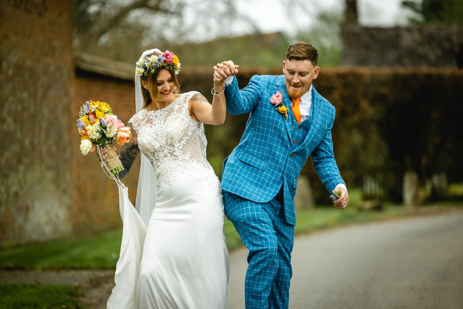 Groom leaping playfully as he leads the bride along a country lane