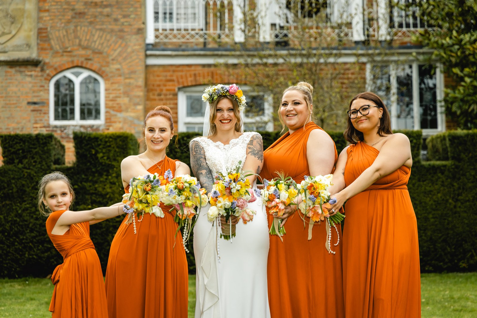 Bride with rust-orange bridesmaids and a flower girl holding colourful bouquets