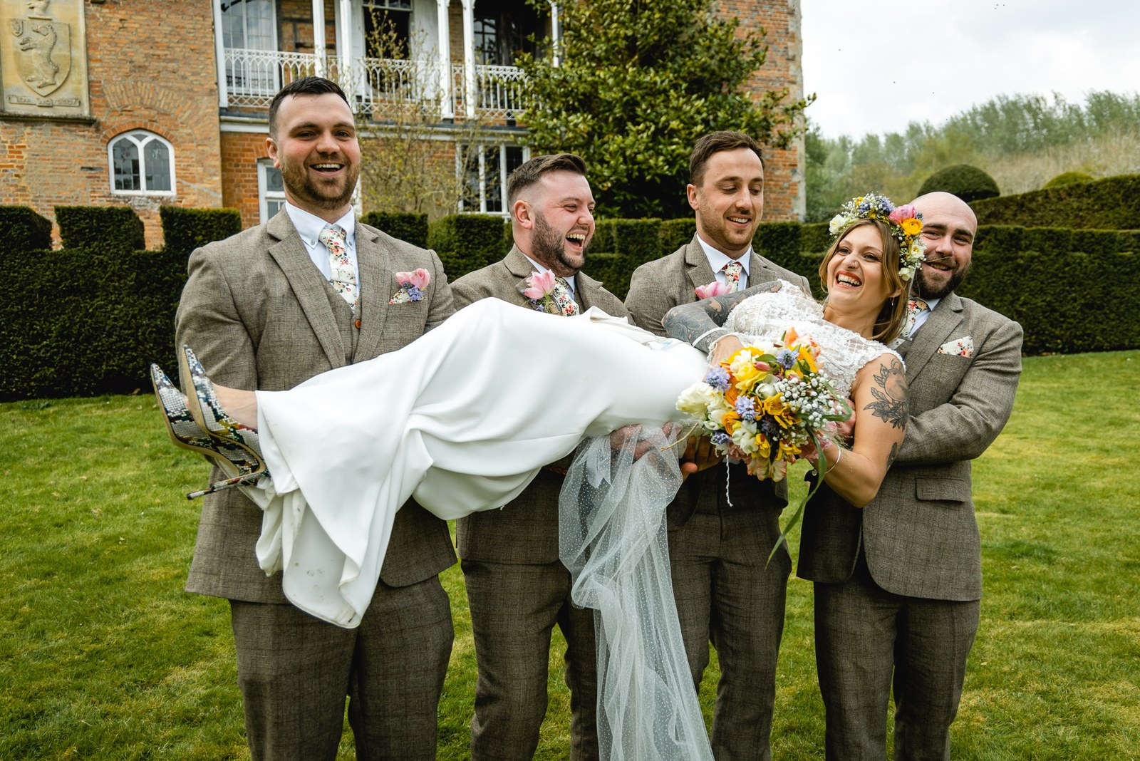 Groomsmen larking about, carrying the bride horizontally on the lawn