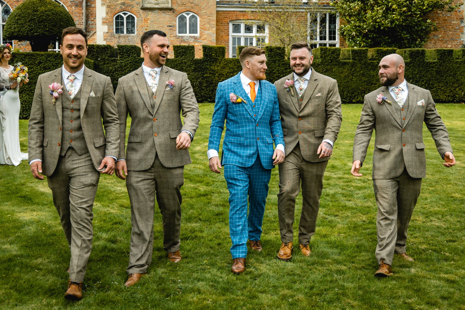 Groom and groomsmen in tweed walking across the lawn, the manor house behind
