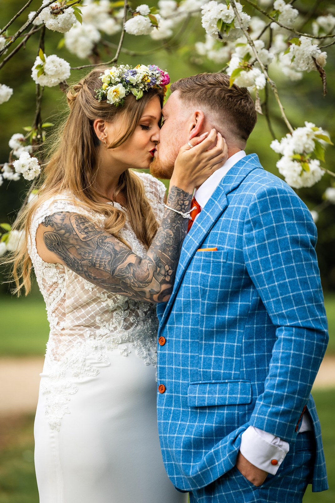 Bride and groom kissing under a blossom-laden tree, the bride in her flower crown