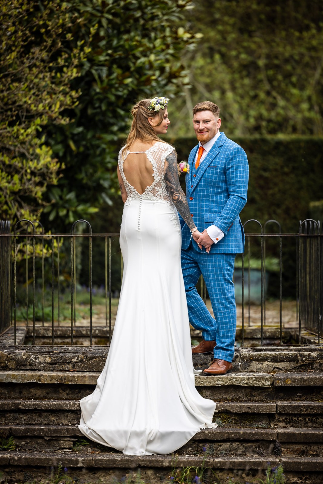 Bride and groom on old stone steps by an iron railing, her low-back gown showing