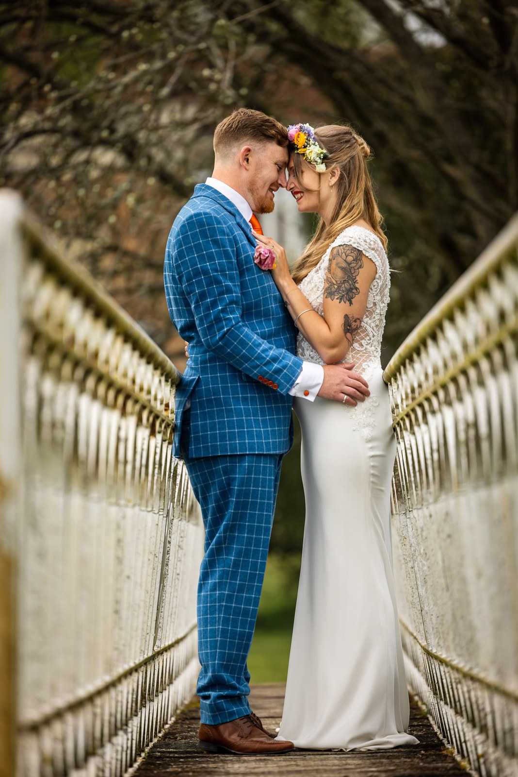 The couple embracing on an ornate white iron footbridge in the grounds