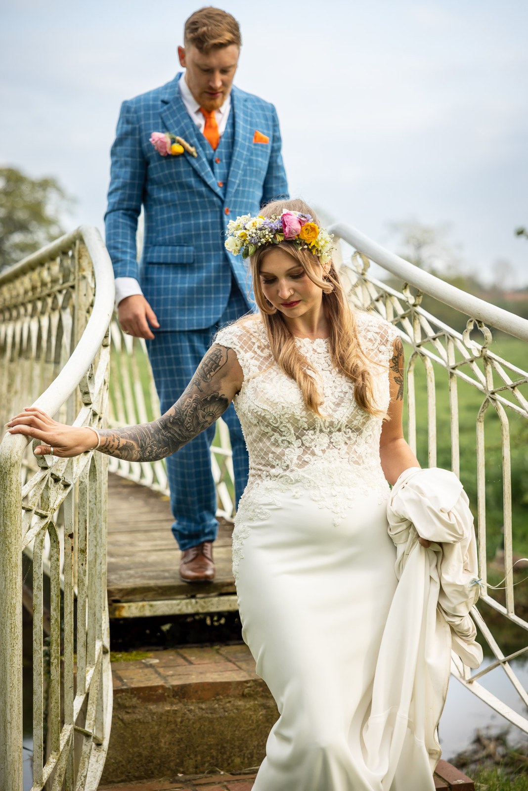 Bride descending the white iron bridge steps holding her dress, groom behind