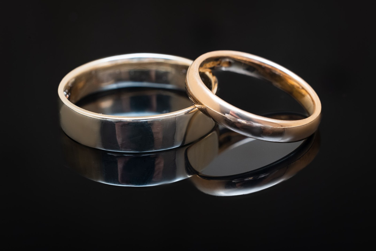 Close-up of two plain wedding bands, one white and one rose gold, on black