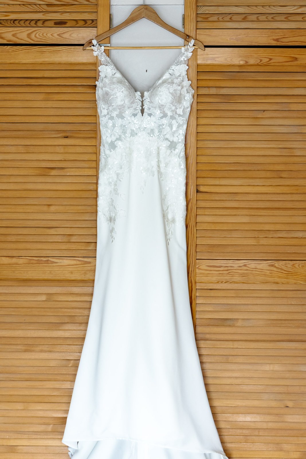Lace wedding dress on a hanger against a pine-clad wall