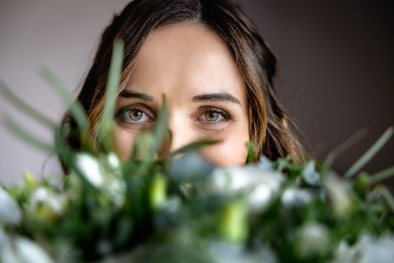 Close-up of the bride's eyes peeking over the foliage of her bouquet