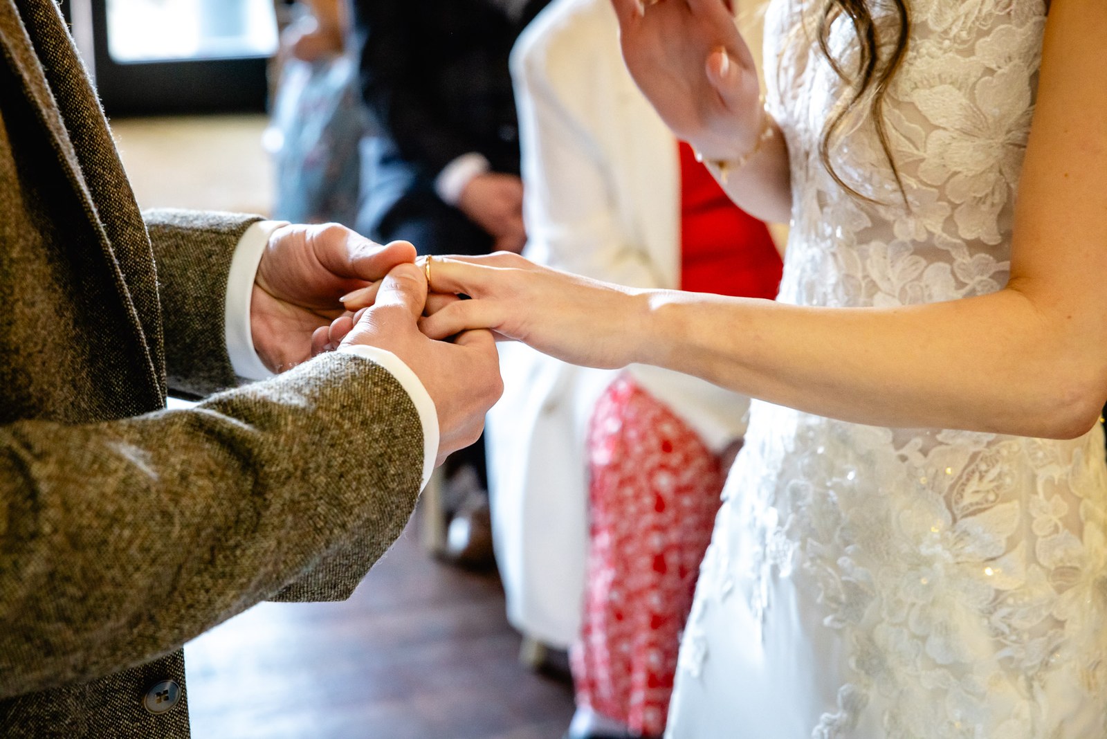 Close-up of the ring exchange, the groom's tweed cuff and the bride's lace gown