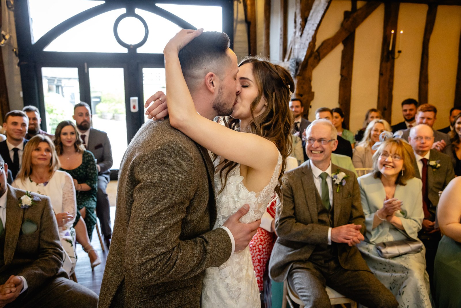 Bride and groom sharing their first kiss in the barn as guests applaud