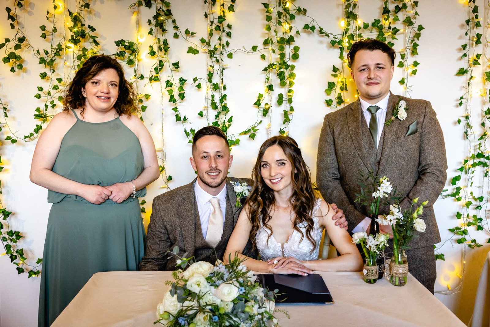 The couple at the signing table against an ivy and fairy-light backdrop