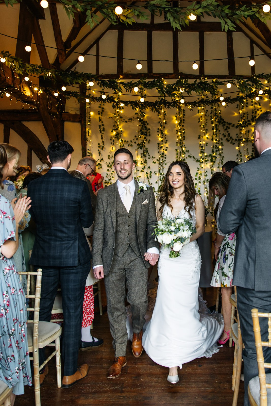 The newlyweds walking back down the aisle beneath the barn's fairy lights and foliage