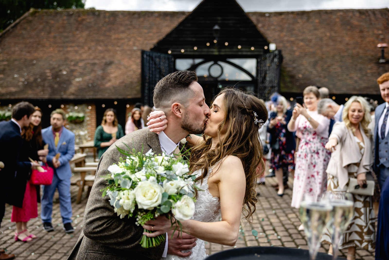 Bride and groom kissing amid confetti in the barn courtyard