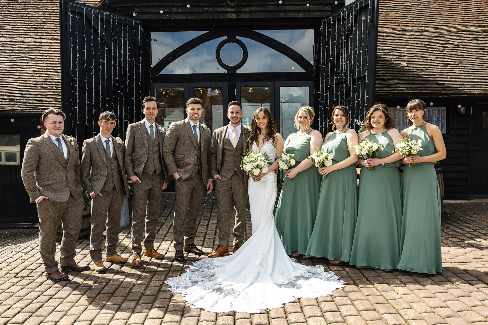 The full bridal party before the black timber frontage of Old Luxters Barn