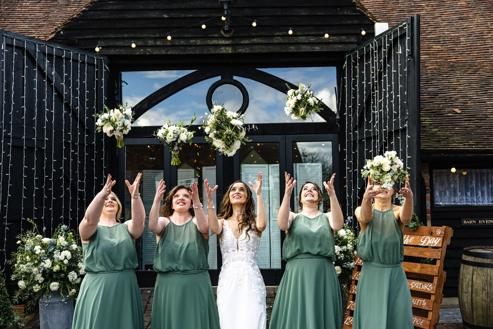 Bride and bridesmaids tossing their bouquets into the air outside the barn