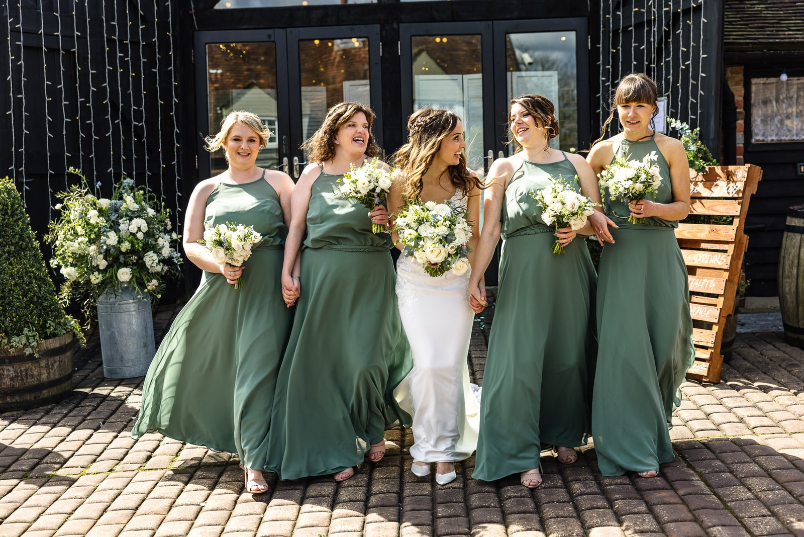 Bride walking with her sage-green bridesmaids in front of the barn