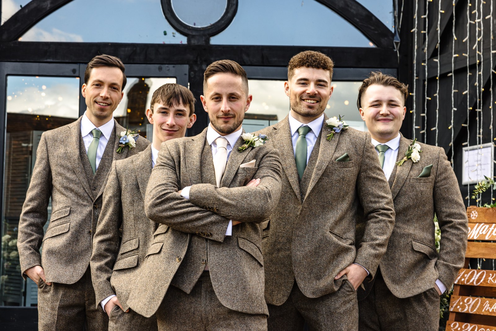Groom and groomsmen in tweed, arms folded, at the barn's glass doors
