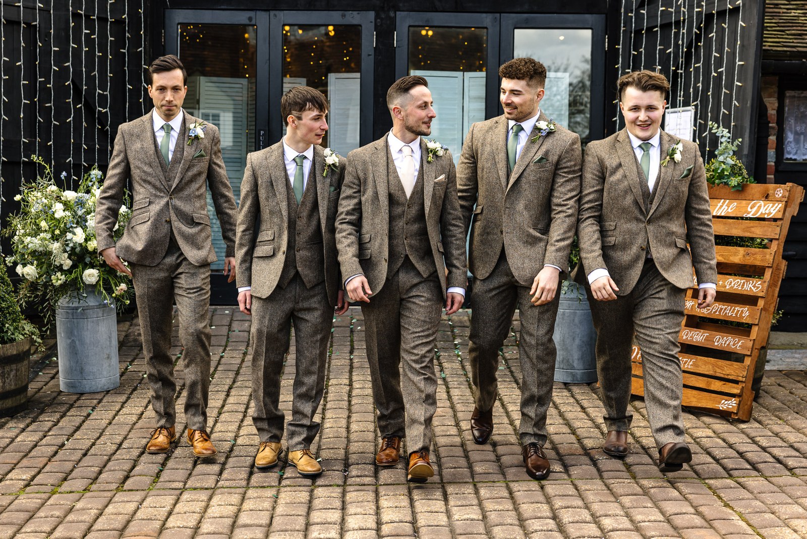 Groom and his groomsmen in tweed walking together outside the barn