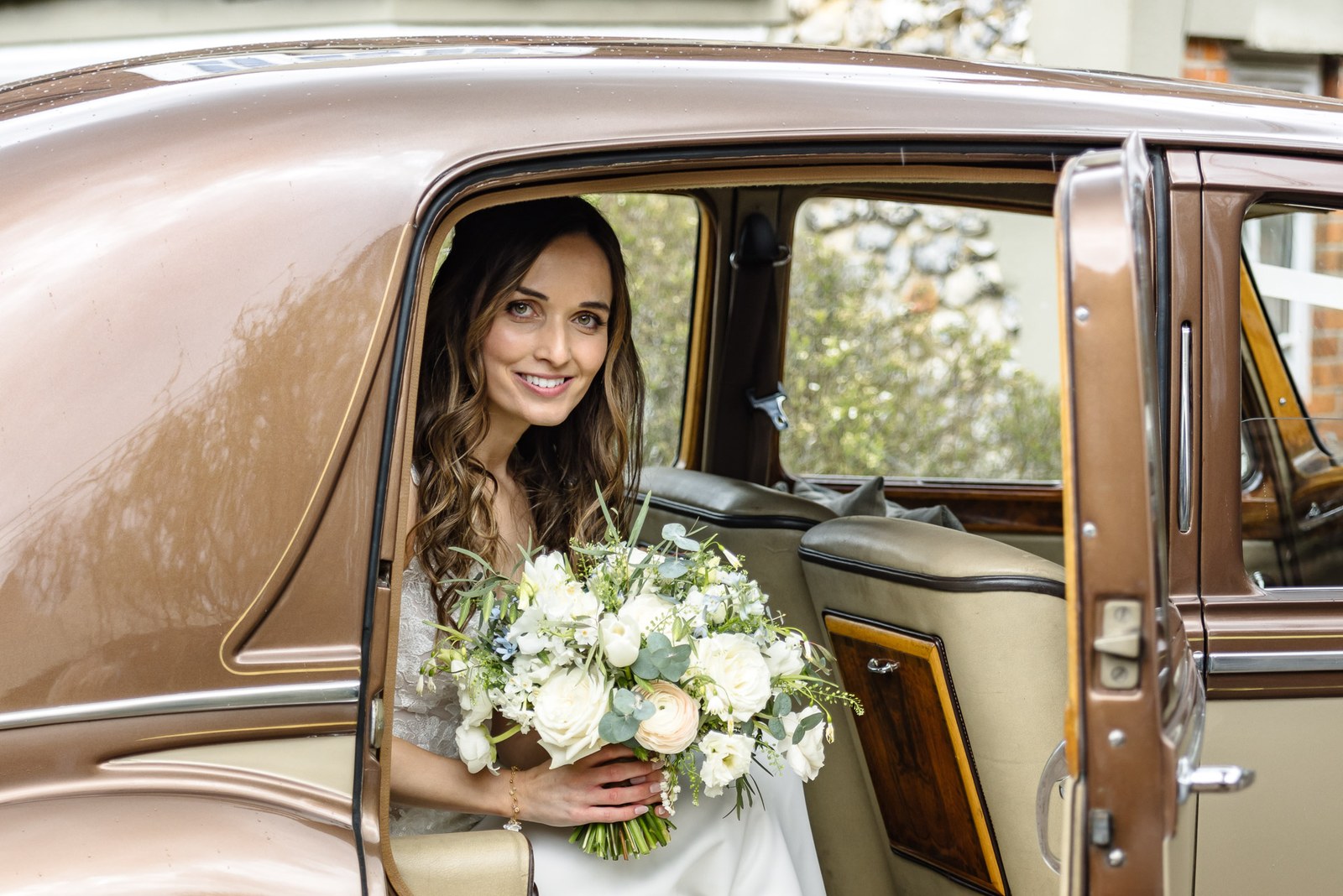 Bride sitting in the doorway of the vintage car holding her bouquet