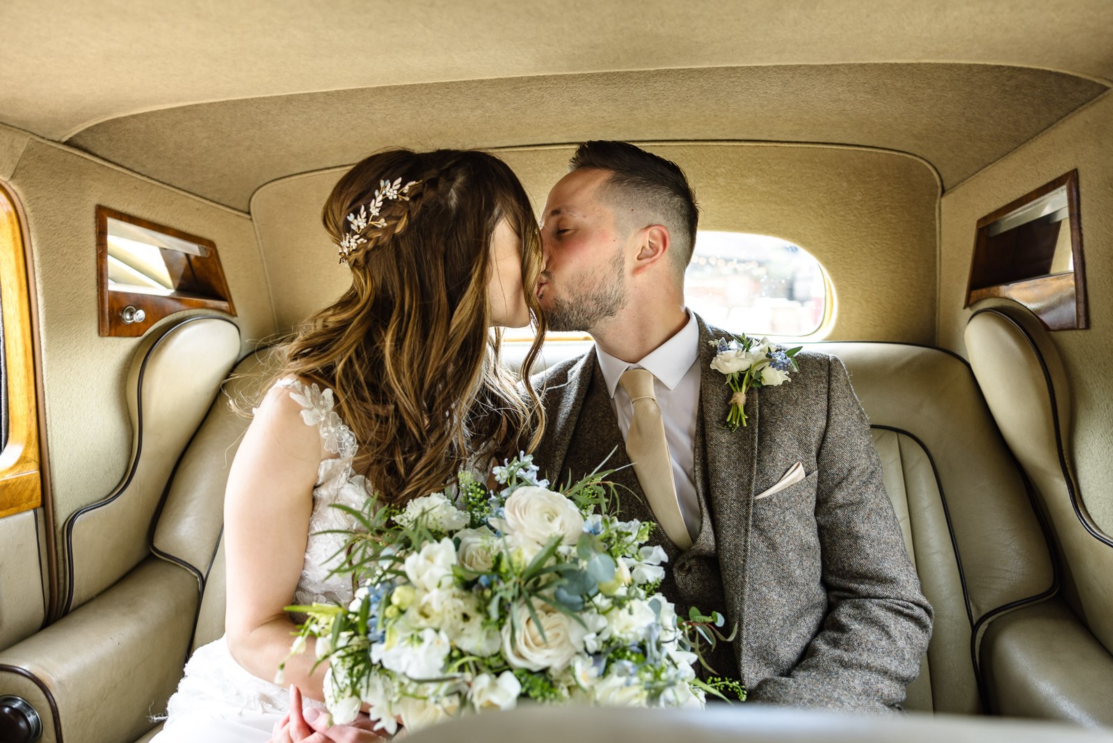 Bride and groom kissing in the back seat of the vintage wedding car