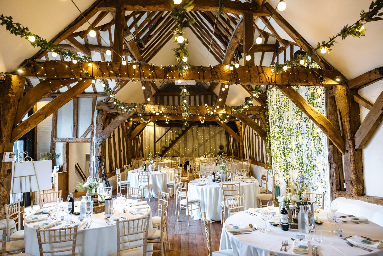 The barn reception at Old Luxters Barn with timber trusses, fairy lights and round tables