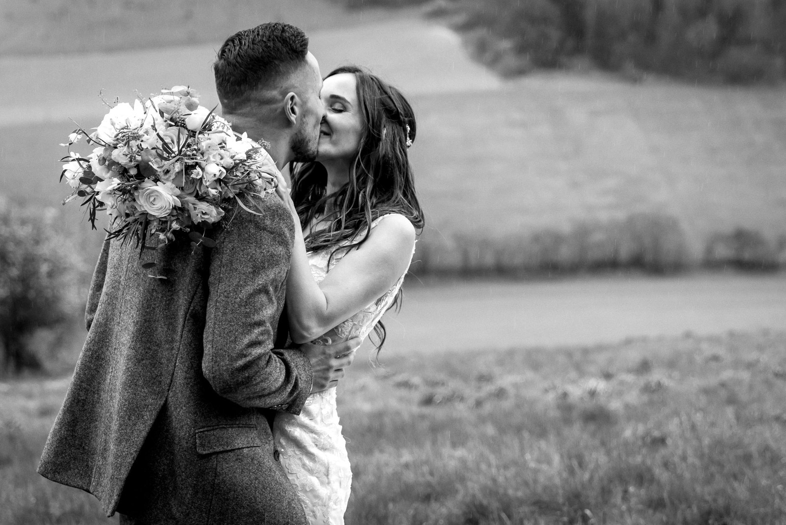 Black and white of the couple kissing in the countryside, bouquet raised