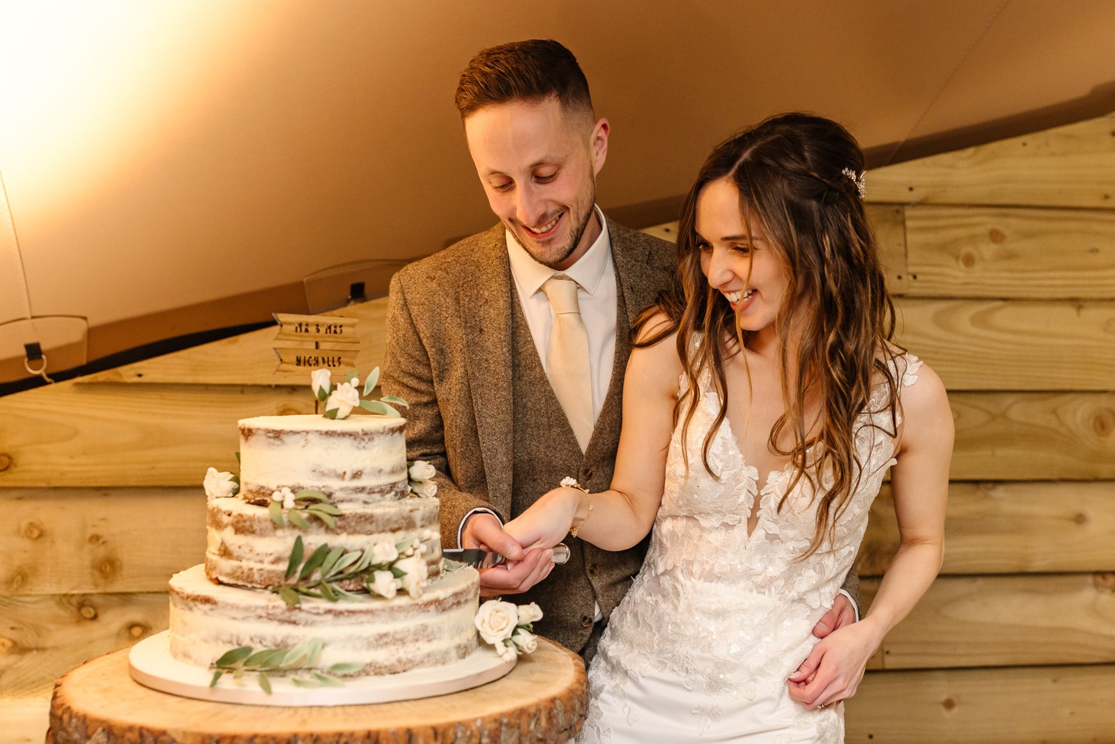 Bride and groom cutting their semi-naked tiered cake on a wood slice