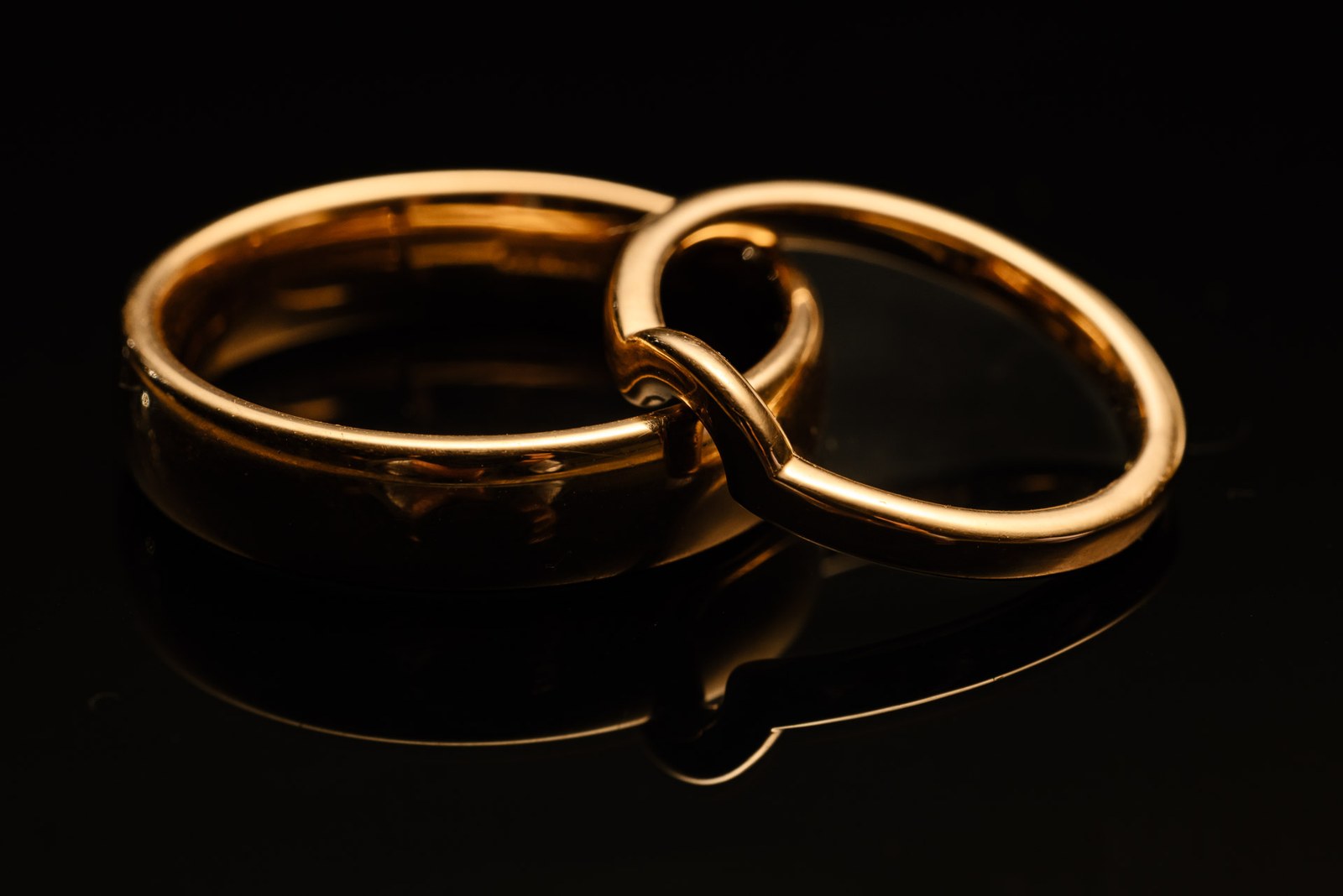 Close-up of two gold wedding bands, one interlinked, on a black surface