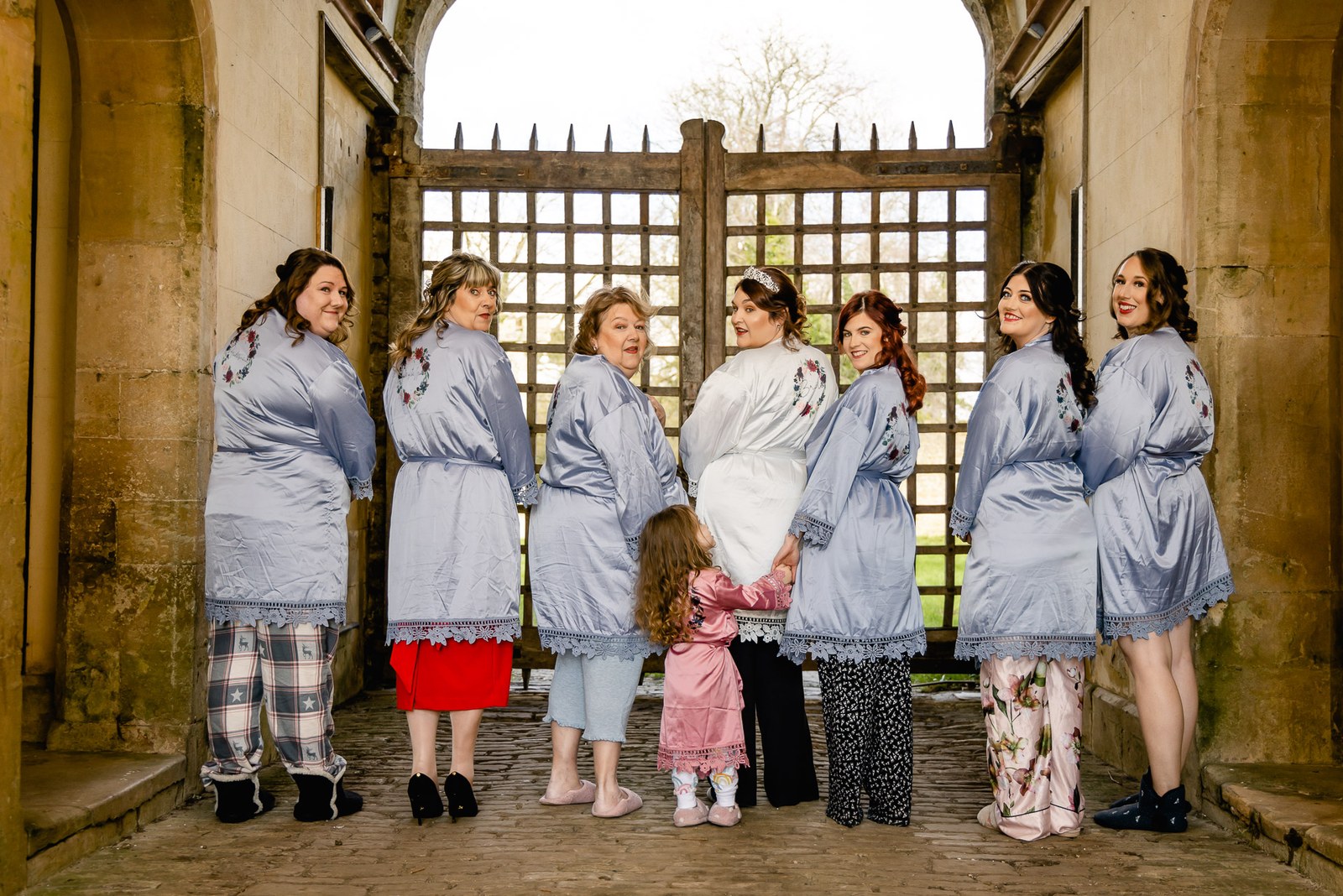Bridesmaids in matching grey satin robes viewed from behind in a stone gateway at Orchardleigh House