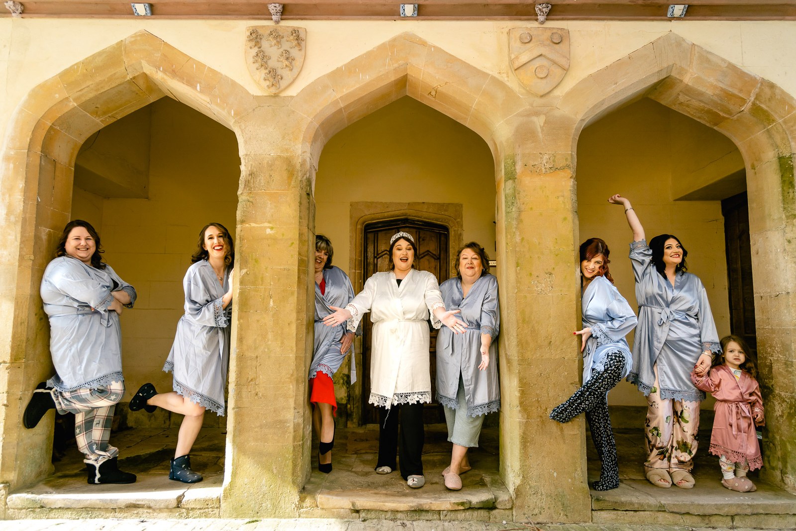 The bridal party posing playfully beneath the Gothic stone arches of Orchardleigh House