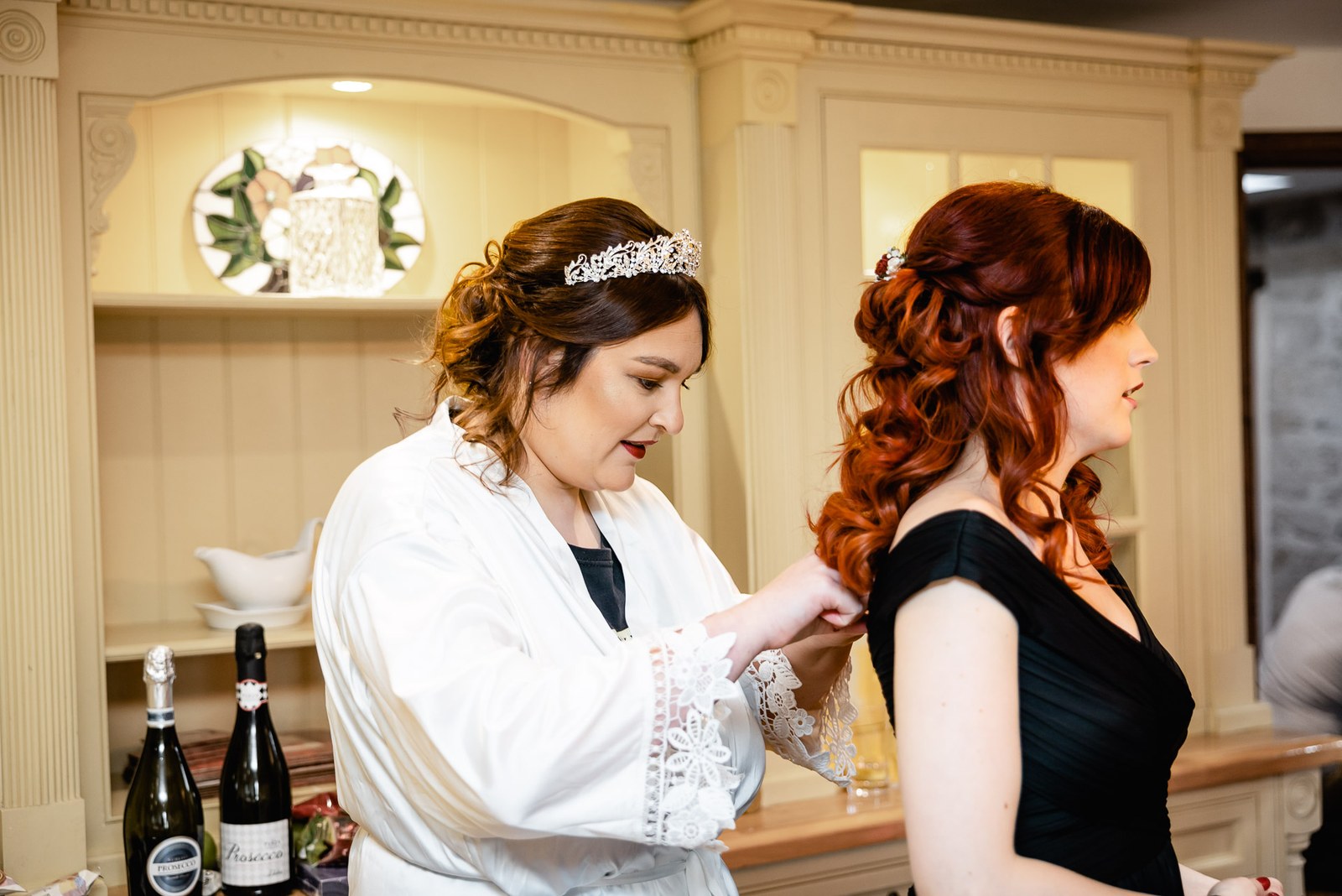 The bride in a white robe fastening a bridesmaid's black dress before the ceremony