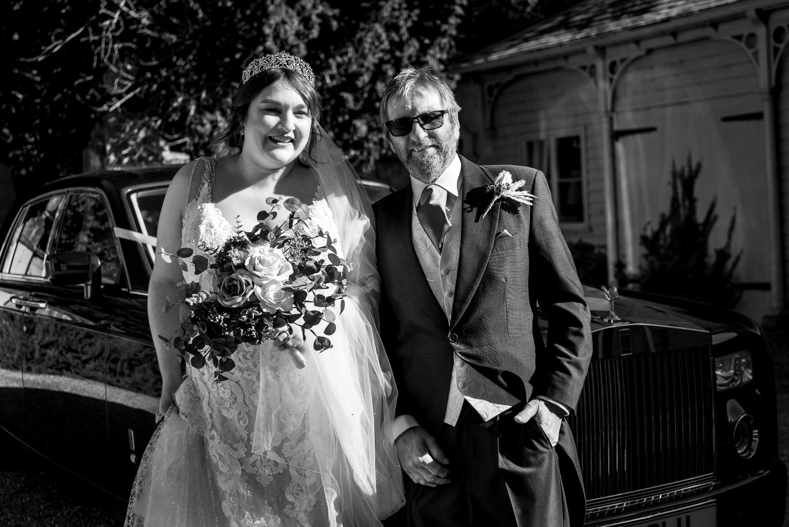 Black-and-white portrait of the bride and her father beside a Rolls-Royce