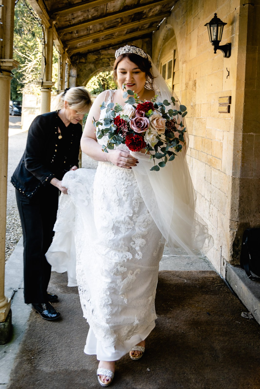 An attendant adjusting the bride's train beneath a stone portico at Orchardleigh House