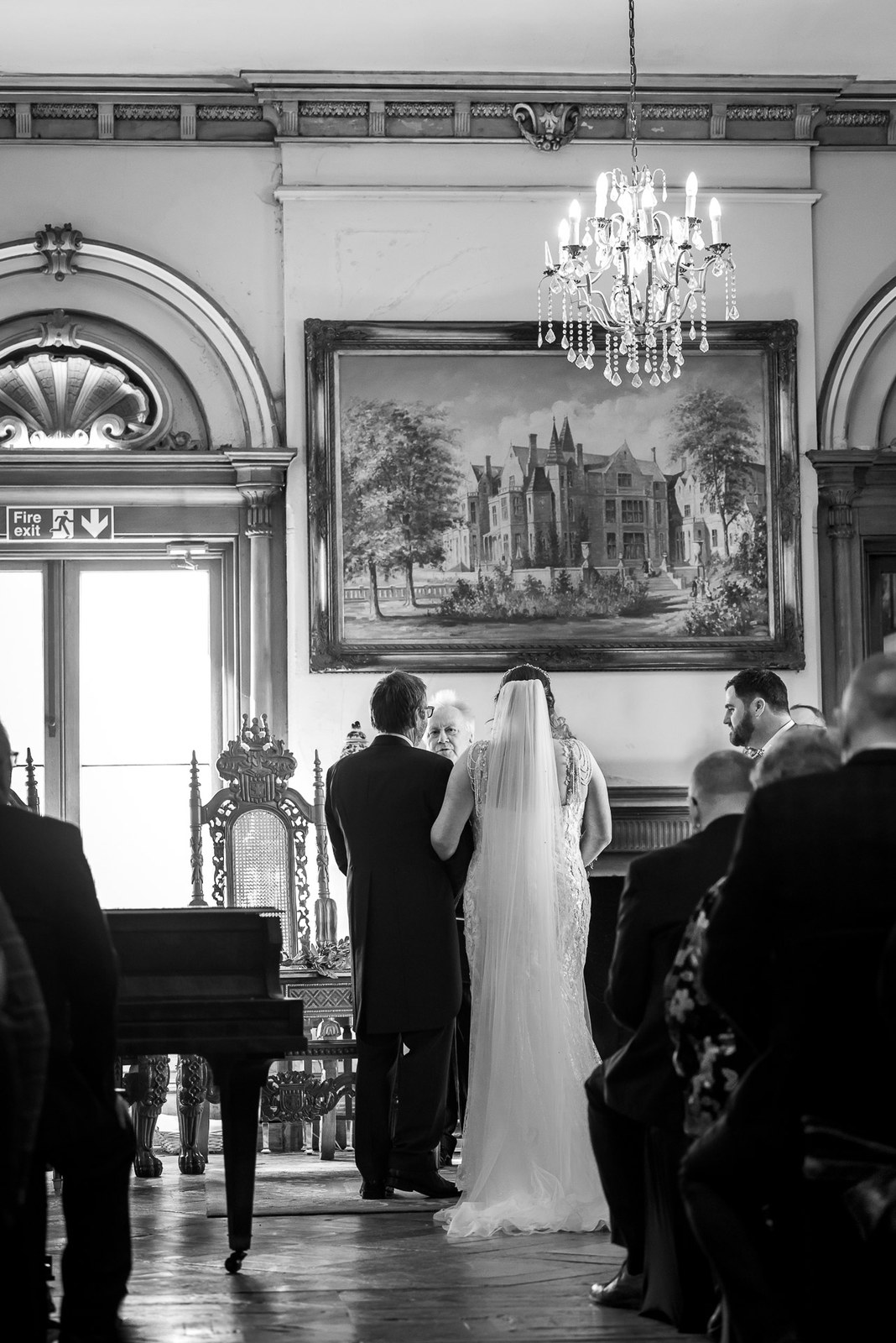 Black-and-white ceremony beneath a chandelier and a painting of Orchardleigh House