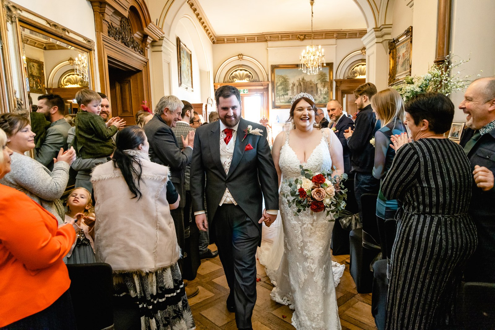 The newlyweds walking back through applauding guests in the grand panelled hall