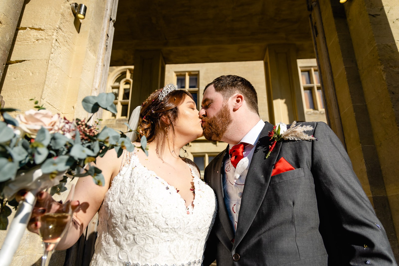 The couple kissing beneath a stone archway, the bride holding her bouquet