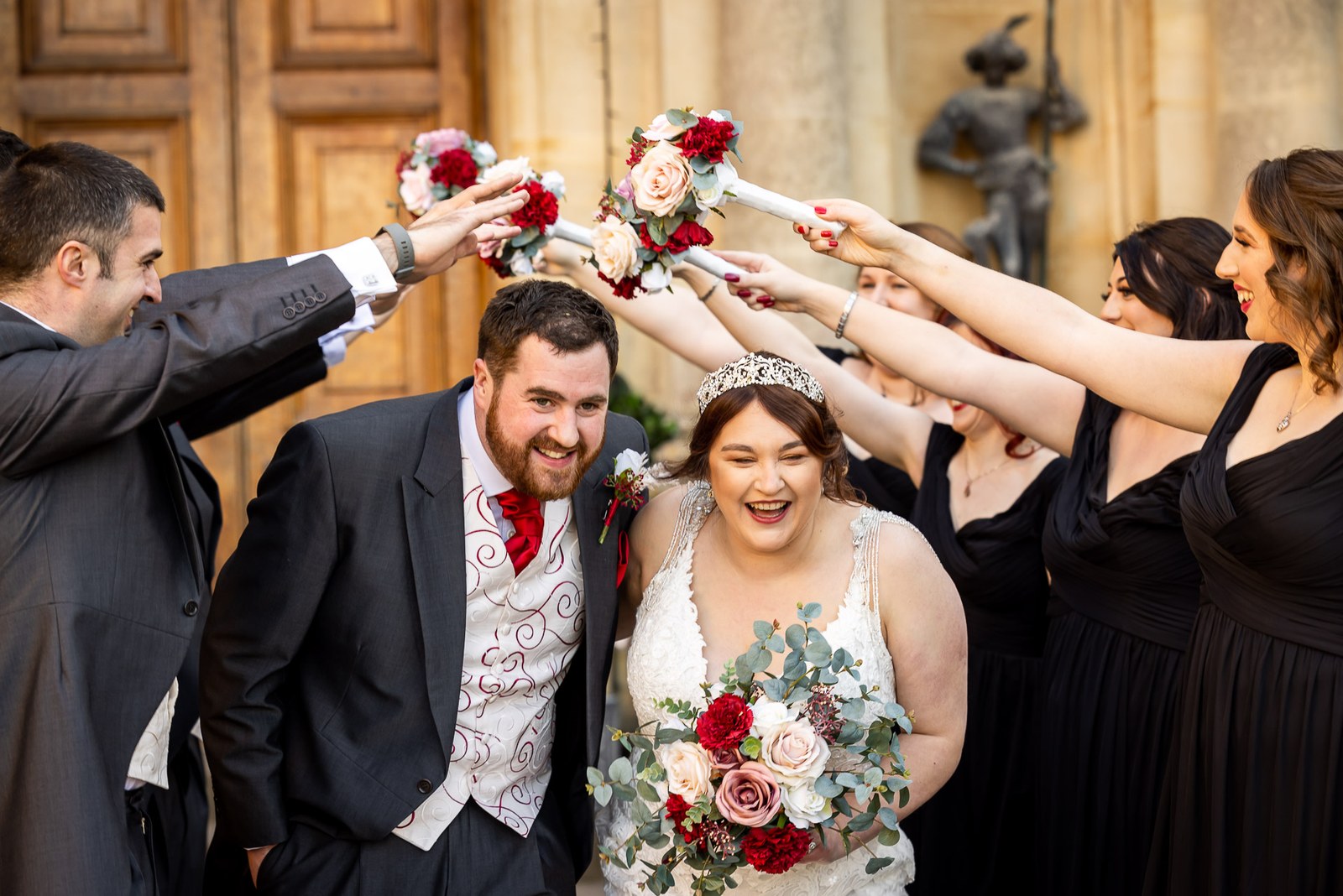 Bridesmaids and groomsmen forming an arch of raised bouquets over the newlyweds