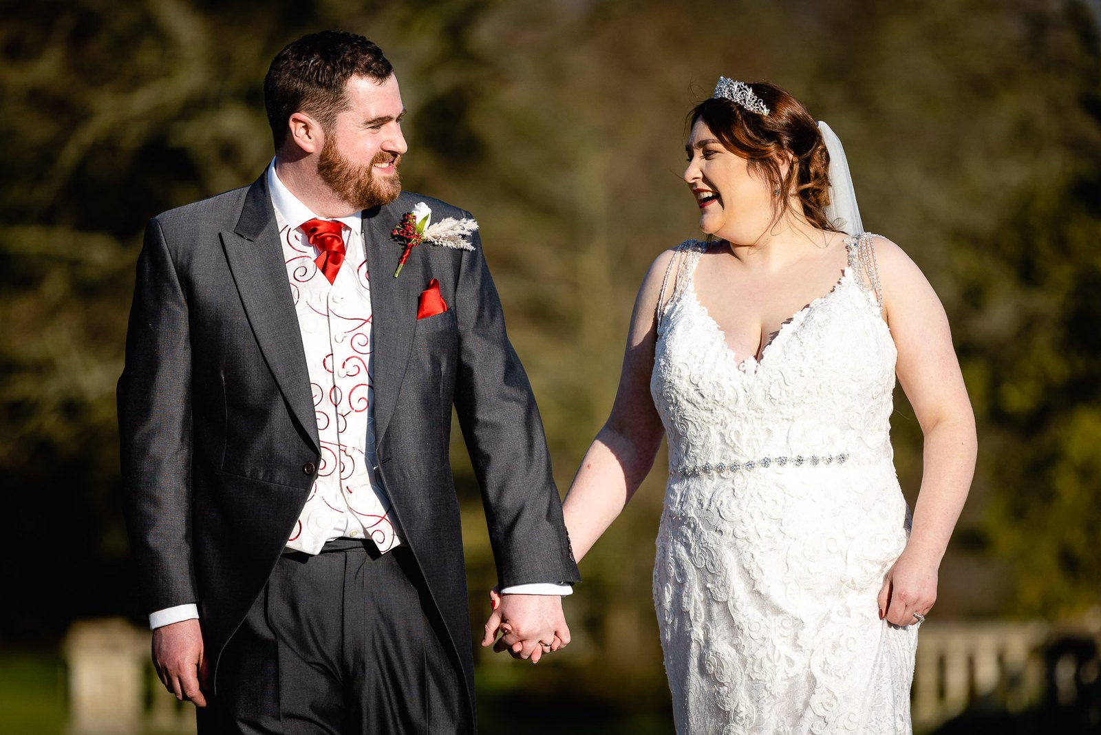 The bride and groom holding hands and smiling at each other in the grounds