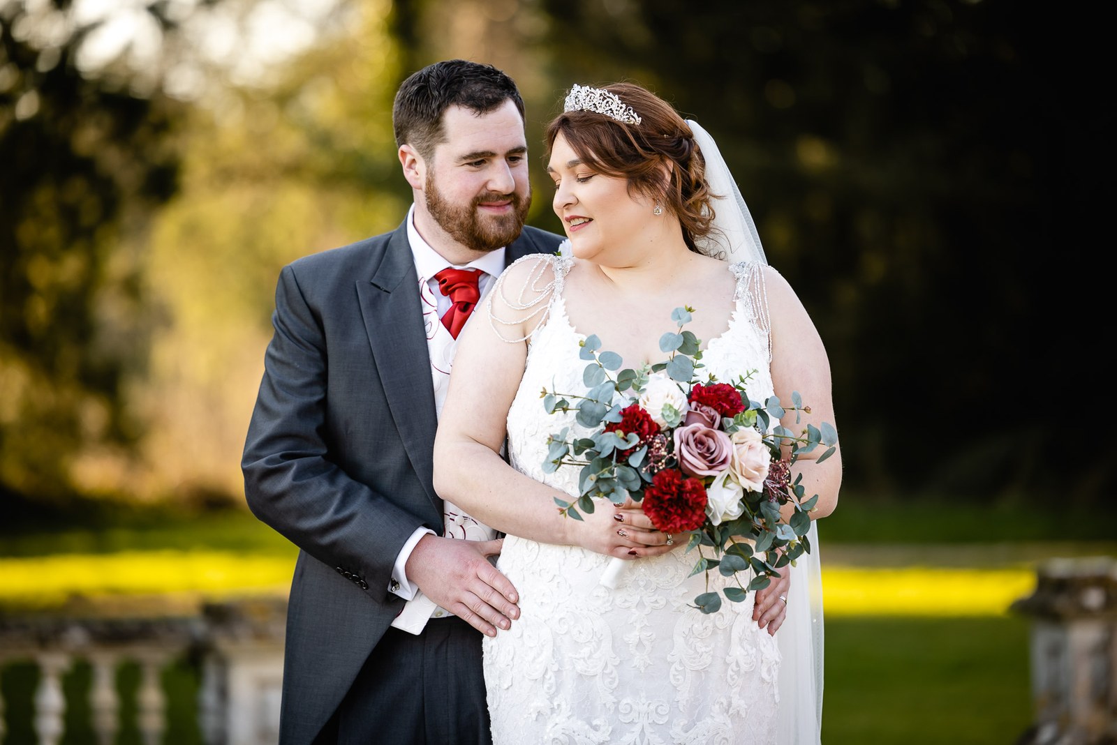 The couple embracing in golden light in the grounds, the bride holding her bouquet