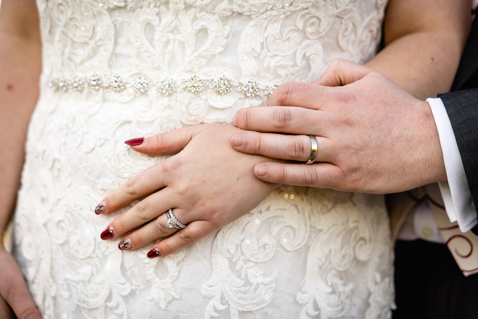 Close-up of the groom's hand resting on the bride's ringed hand with red nails over her beaded gown