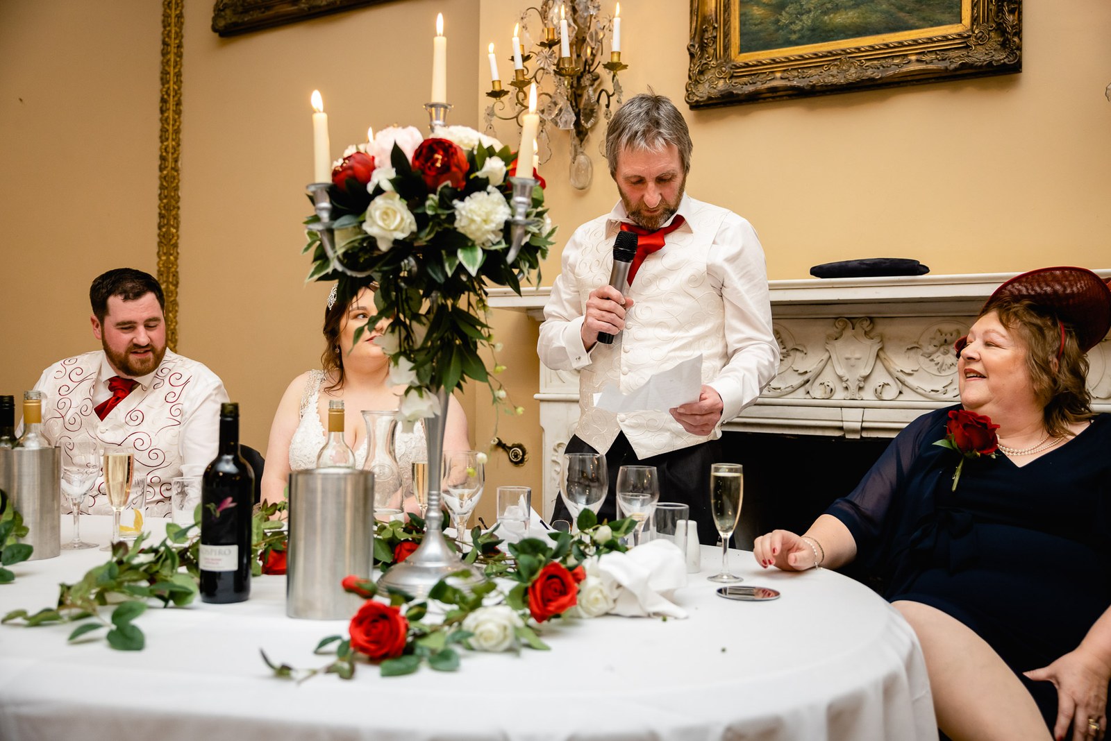 A speaker addressing the top table beside a tall red and white floral centrepiece