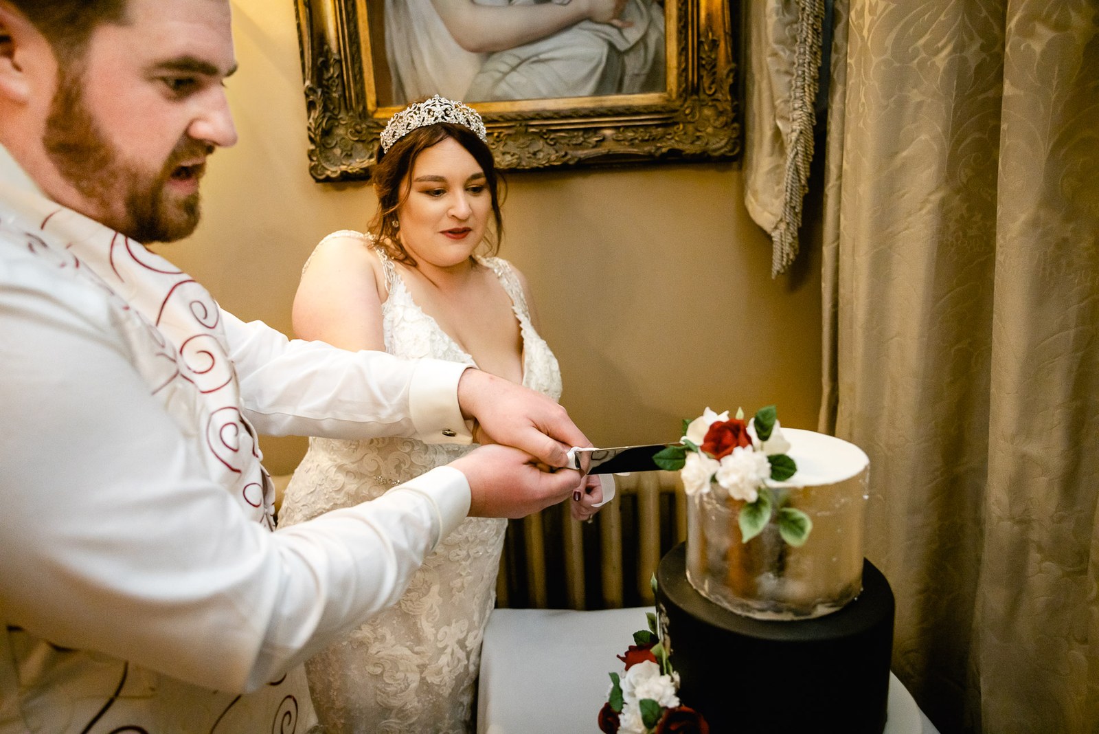 The couple cutting a small tiered wedding cake trimmed with roses