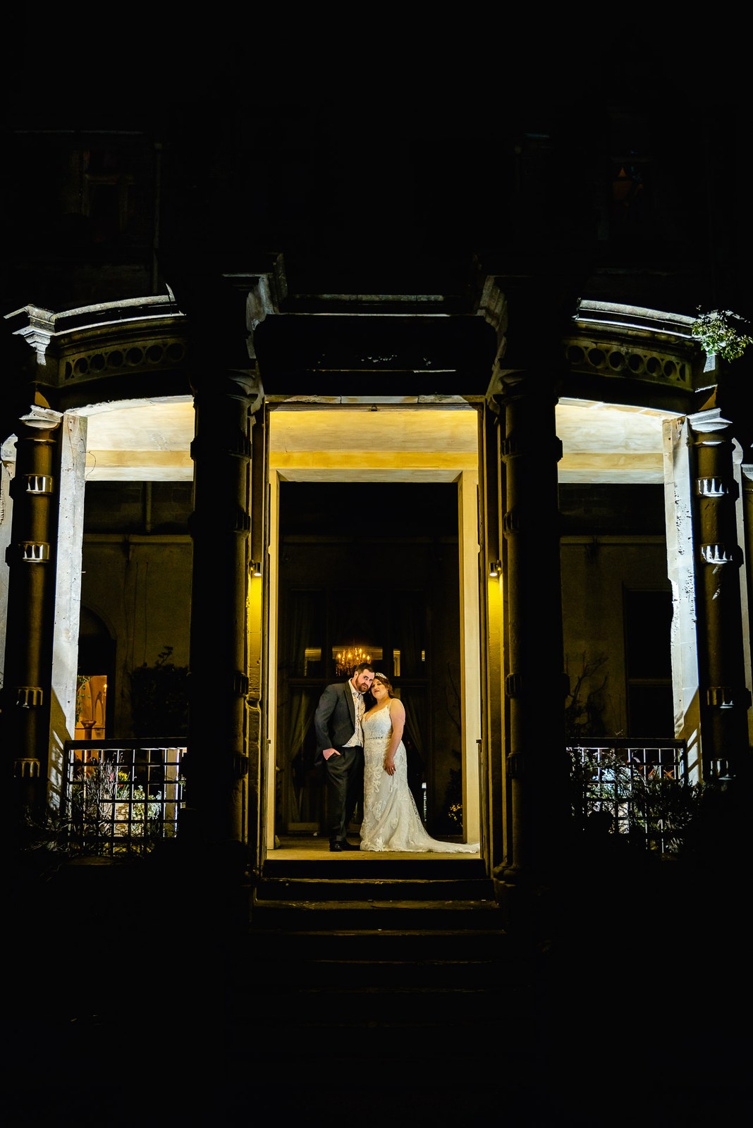 The couple leaning together in the lit doorway of Orchardleigh House against the dark night facade