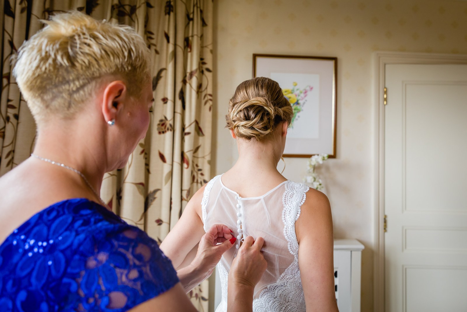 A woman fastening the back of the bride's gown in the suite